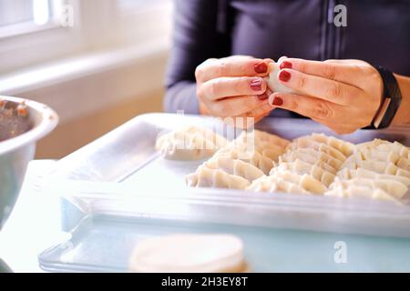 Schöne Dame Hände machen Fleisch Knödel auf Tisch neben Fenster in der Küche zu Hause. Stockfoto