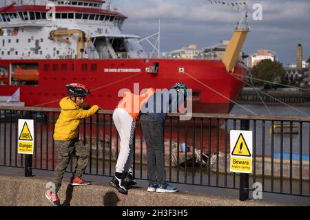 Junge Londoner bewundern das neue Polarforschungsschiff der British Antarctic Survey, das RRS Sir David Attenborough, das auf der Themse am Prime Meridian, Greenwich, vor Anker liegt, während seines kurzen Aufenthalts, der der Öffentlichkeit während der COP26-Klimakonferenz in Glasgow am 28. Oktober 2021 in London gezeigt wurde, England. Der £200m Attenborough ist ein Eisbrecher der Polar-Klasse 4 mit modernster Forschungsausrüstung, einem Hubschrauberlandeplatz, Kränen, Laboren an Bord und anderen Geräten für die Ozeanuntersuchung und Probenahme. Er liegt an der Themse am Prime Meridian, Greenwich, während seines kurzen Aufenthalts, der im Pub gezeigt wird Stockfoto