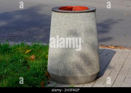 Neben dem Rasen, auf dem Bürgersteig in der Nähe der Straße im Wohnbezirk Goclaw in Warschau, Polen, wurde ein Abfalleimer aus Beton aufgestellt. Stockfoto