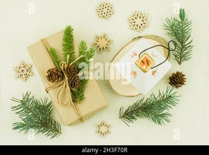 Weihnachten gestrickter Hintergrund mit einem Geschenk aus Kraftpapier, einer Kerze in einem keramischen Kerzenständer, Fichtenzweigen. Draufsicht Stockfoto