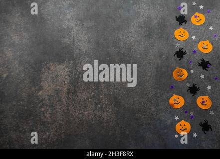 Halloween Hintergrund: Konfetti in Form von orangefarbenen Kürbissen mit lustigen Gesichtern, schwarzen Spinnen und Sternen. Grauer Hintergrund. Speicherplatz kopieren. Stockfoto