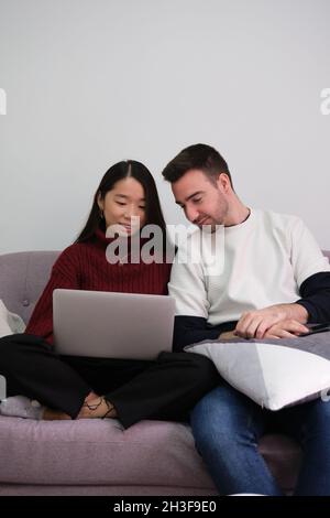 Junges Paar, das sich zu Hause mit einem Laptop auf der Couch entspannt. Stockfoto