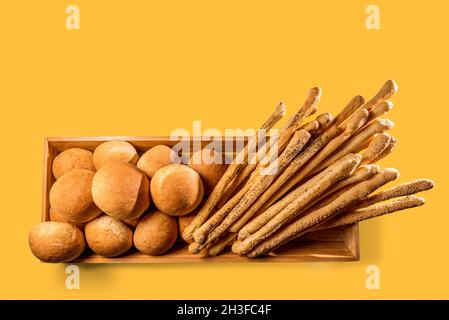 Knusprige Brötchen, Brotstäbchen mit Sesam und Mohn in Holzschale, isoliert auf gelbem Hintergrund in der Draufsicht, Kopierraum Stockfoto