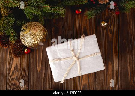 Minimalistisches, umweltfreundliches, eingewickeltes weihnachtsgeschenk auf einem Holztisch mit Tannenzweigen und Christmassenkugeln. Stockfoto