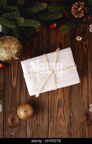 Minimalistisches, umweltfreundliches, eingewickeltes weihnachtsgeschenk auf einem Holztisch mit Tannenzweigen und Christmassenkugeln. Stockfoto