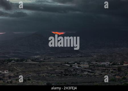 Schwere Sturmwolken in der Dämmerung über den Bergen. Ein Stück rote Sonnenscheibe kann durch die Wolken gesehen werden. Spanien, busot Gebiet, Alicante Provinz.Horizontal Stockfoto