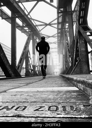 Vertikale Aufnahme einer Person, die unter einer Eisenbahnbrücke läuft. Stockfoto