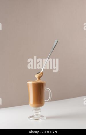 Glasbecher mit Cappuccino und duftendem Schaum und Löffel. Tasse mit Cappuccino, Latte oder Kaffee mit Milch. Kreatives Design für Cafés und Restaurants mit Stockfoto