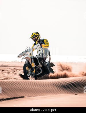 Motocross-Fahrer, der in Sanddünen mit herrlichen Palmen und dem Meer im Hintergrund in Bibione, Italien, an einem stimmungsvollen und hellen Tag fährt. Stockfoto