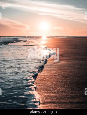 Herrlicher Sonnenuntergang in Italien, Bibione, am Meer mit herrlichem Licht und Wellen vorne, die sich in eine wunderschöne romantische Landschaft vermischen. Stockfoto