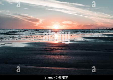 Herrlicher Sonnenuntergang in Italien, Bibione, am Meer mit herrlichem Licht und Wellen vorne, die sich in eine wunderschöne romantische Landschaft vermischen. Stockfoto