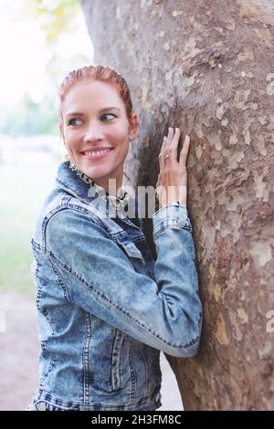Junge kaukasische Rotschopf Frau berühren Baum im Park, Natur Stockfoto