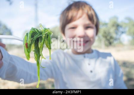 Kleiner Junge mit Wakame-Salat auf der Gabel. Außenhintergrund Stockfoto