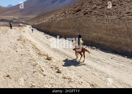 Kagbeni, Mustang District, Nepal - 19. November 2016: Nepalesischer Reiter auf einem Pferd reitet auf einer Straße im Himalaya. Muktinath Sadak Stockfoto