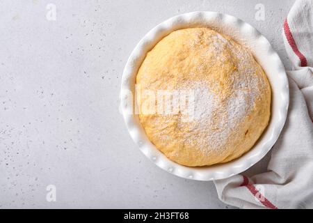 Roher Hefeteig mit Kürbis in weißer Schüssel mit Handtuch auf dem bemehlten Küchentisch bedeckt, Rezeptidee. Konzept Hausbacken Brot, Brötchen oder Cinnabon o Stockfoto