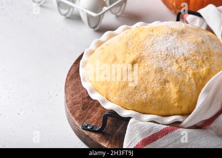 Roher Hefeteig mit Kürbis in weißer Schüssel mit Handtuch auf dem bemehlten Küchentisch bedeckt, Rezeptidee. Konzept Hausbacken Brot, Brötchen oder Cinnabon o Stockfoto