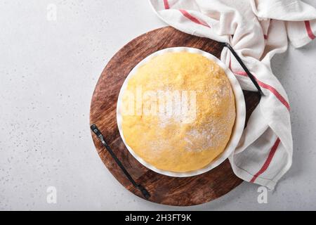 Roher Hefeteig mit Kürbis in weißer Schüssel mit Handtuch auf dem bemehlten Küchentisch bedeckt, Rezeptidee. Konzept Hausbacken Brot, Brötchen oder Cinnabon o Stockfoto