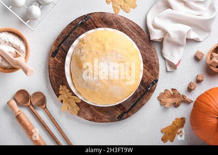 Roher Hefeteig mit Kürbis in weißer Schüssel mit Handtuch auf dem bemehlten Küchentisch bedeckt, Rezeptidee. Konzept Hausbacken Brot, Brötchen oder Cinnabon o Stockfoto