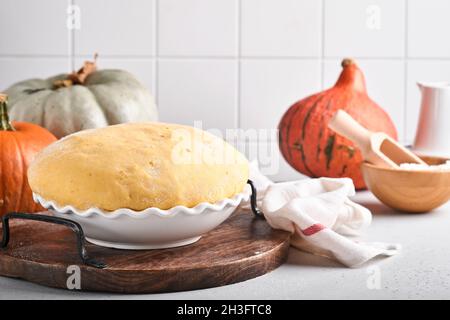 Roher Hefeteig mit Kürbis in weißer Schüssel mit Handtuch auf dem bemehlten Küchentisch bedeckt, Rezeptidee. Konzept Hausbacken Brot, Brötchen oder Cinnabon o Stockfoto