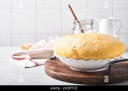 Roher Hefeteig mit Kürbis in weißer Schüssel mit Handtuch auf dem bemehlten Küchentisch bedeckt, Rezeptidee. Konzept Hausbacken Brot, Brötchen oder Cinnabon o Stockfoto