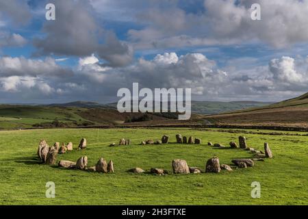 Swinside aka Sunkenkirk Steinkreis; helle Nachmittagssonne; blauer Himmel mit grauen und weißen Wolken; Felder, Moorland, Hügel und Zufahrtsweg in Backgrou Stockfoto