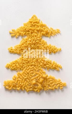 Alternativer Weihnachtsbaum aus trockener italienischer Pasta auf weißem Hintergrund. Vertikale Weihnachtskarte. Blick von oben. Konzept für Essens- und Urlaubsreise. Stockfoto