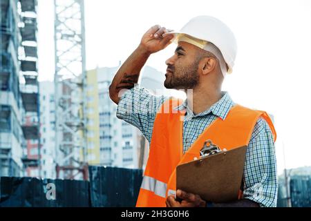 Junger Mann Ingenieur in Arbeitskleidung steht auf der Baustelle mit Zwischenablage Stockfoto