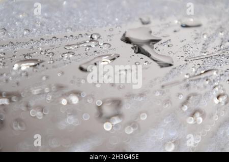 Silbernes Makro aus feuchter, verschwommener Spiegelglas-Oberfläche mit Reflexion und Wassertropfen. Selektiver Fokus und Unschärfe Stockfoto