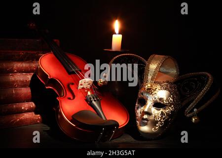 Schöne Violine neben venezianischer Maske und Kerze auf schwarzem Hintergrund Stockfoto