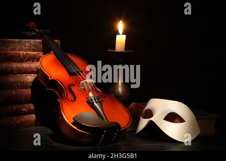 Schöne Violine neben venezianischer Maske und Kerze auf schwarzem Hintergrund Stockfoto