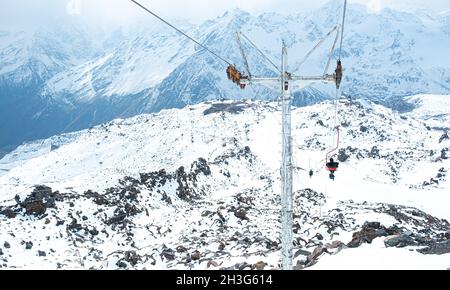 Menschen auf der Seilbahn vor dem Hintergrund schneebedeckter Berggipfel. Skigebiet. Sessellift für Touristen, Snowboarder und Skifahrer. Elbrus Stockfoto