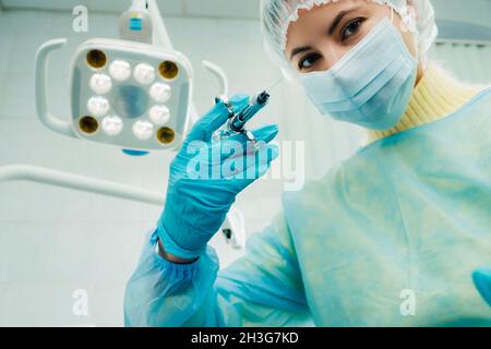 Ein maskierter Zahnarzt hält eine Injektionsspritze für einen Patienten im Büro. Stockfoto