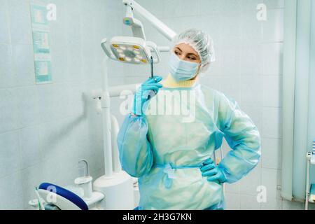 Ein maskierter Zahnarzt hält eine Injektionsspritze für einen Patienten im Büro. Stockfoto