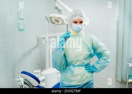 Ein maskierter Zahnarzt hält eine Injektionsspritze für einen Patienten im Büro. Stockfoto