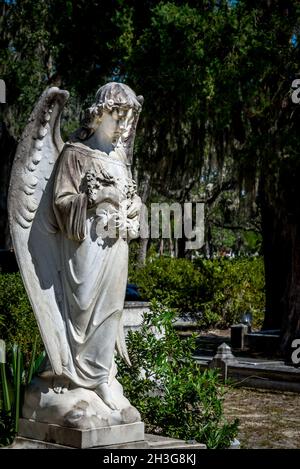 Steinstatue eines Engels, der Blumen vor einem Hintergrund mit Bäumen hält Stockfoto