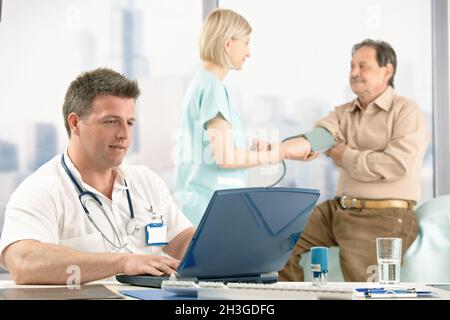 Arzt am Schreibtisch, Krankenschwester, die den Patienten untersucht. Stockfoto