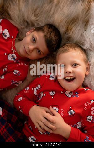 Glückliche Brüder im Pyjama liegen auf dem Teppich von weihnachtsbaum und haben Spaß mit Freude an weihnachten. Kaukasische Kinder zu Hause in den weihnachtsferien Stockfoto