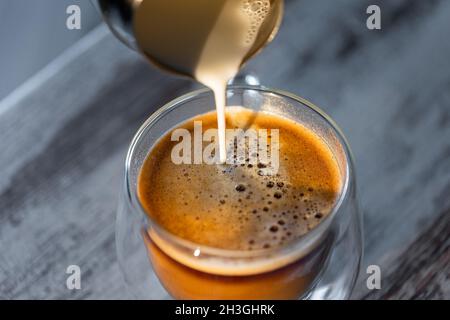 Milch wird in eine Tasse Kaffee gegossen. Morgens erfrischender Kaffee Stockfoto