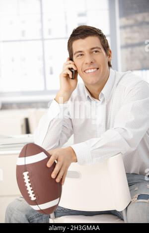 Glücklicher Geschäftsmann am Telefon, mit Fußball Stockfoto