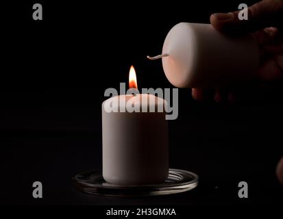 Brennende Kerze mit Flamme, Menschenhände zünden Kerze an, schwarzer Hintergrund. (Fokus auf Kerze). Stockfoto