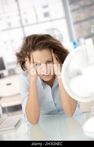 Junge Frau, die vor einem Ventilator sitzt und sich abkühlt Stockfoto