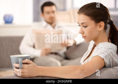 Junge Frau sitzt auf dem Sofa Mann im Hintergrund Stockfoto