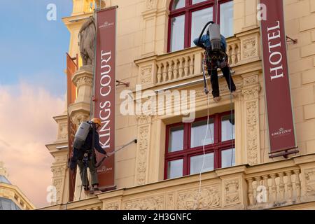 Prag, CZ - 28. oktober 2021:zwei Arbeiter mit Staubsaugern, die hoch oben auf der Rupe hängen und Staub an der Fassade eines Hotels in Prag reinigen. Sauber Stockfoto