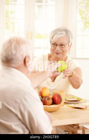 Lächelnde ältere Frau, die dem Ehemann Apfel überreicht Stockfoto
