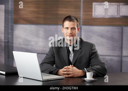 Selbstbewusster Manager, der lächelnd in einem schicken Büro sitzt Stockfoto