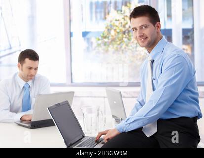 Junger Geschäftsmann mit Laptop lächelt im Büro Stockfoto