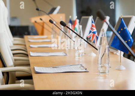 Politische Berichte in den auf dem Konferenztisch mit Glasflaschen, Nationalflaggen und Mikrofonen angebrachten Klemmbrettern Stockfoto