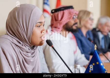 Selbstbewusste junge muslimische Politikerin im Hijab spricht ins Mikrofon, während sie die Frage der Journalistin stellt Stockfoto