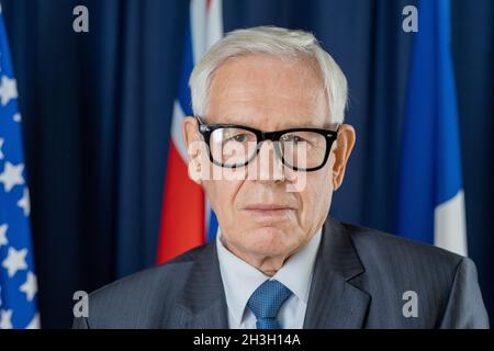 Porträt eines seriös selbstbewussten hochrangigen Politikers in Brillen, die gegen Flaggen und dunkelblaue Vorhänge stehen Stockfoto