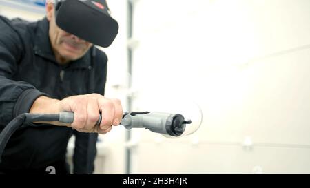 VR-Technologien in der Fertigungsindustrie. Szene. Arbeiter in virtuellen Gläsern hält Spritzpistole und malt Maschinenteil. Fabrikarbeiter nutzt virtuell Stockfoto